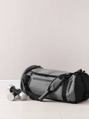 Grey sports bag and dumbbells on floor near light wall, space for text